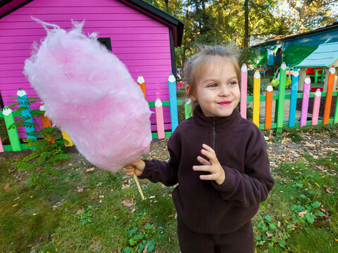 Happy little girl holding a huge pink cotton candy outdoors.