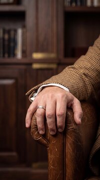 Close Up of Elegant Gentleman Hand with Wedding Ring Resting on Vintage Leather Armchair