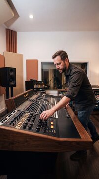 Male sound engineer adjusting knobs on a large vintage analog mixing console in a professional music recording studio