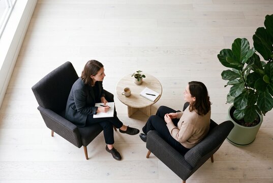 Two businesswomen or a therapist and client having a professional consultation in a minimalist office with comfortable armchairs