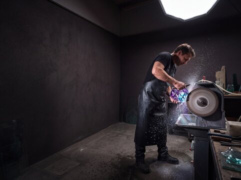 Skilled Male Artisan Grinding and Polishing a Faceted Glass Sculpture on Lapidary Wheel in Workshop