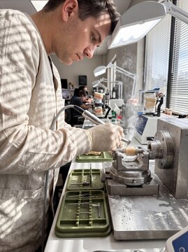 Dental technician carving and shaping a ceramic tooth prosthesis with a precision handpiece drill in a laboratory