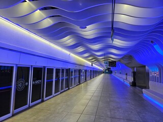 Fototapeta premium ISTANBUL - APR 10, 2026: Modern subway station with blue-lit wavy ceiling. Glass doors line the platform. Bright lights illuminate the curved architecture. Clean, sleek, and futuristic design