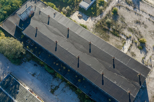 Aerial view of an old warehouse with a flat roof and multiple chimneys, surrounded by paved areas and sparse vegetation in Warszawa, Mazowieckie, Poland.