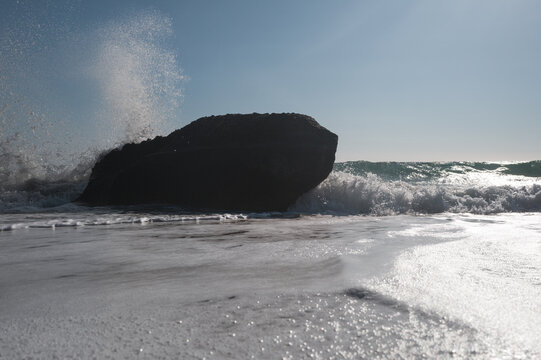 Sea surf on a coast with black stones in the water, viewed against strong backlight.