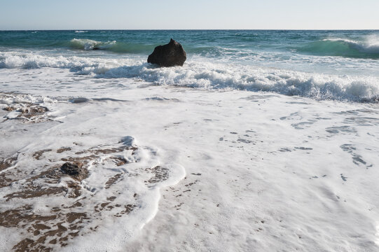 Sea surf on a coast with black stones in the water, viewed against strong backlight.
