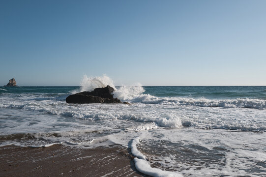 Sea surf on a coast with black stones in the water, viewed against strong backlight.