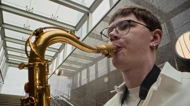 Young adult Caucasian man playing saxophone in urban pedestrian underpass in slow motion with zoom out. Clip perfect for music festival advertising and city culture campaigns