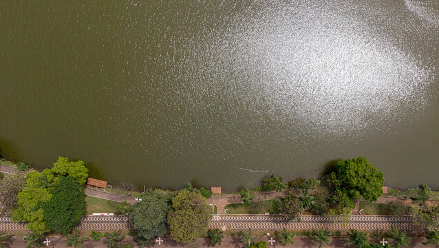 Aerial view of Parque Municipal Fabio da Silva Prado - Lago Municipal with lush trees, a paved walking path, and sunlight reflecting on the water in Araras, Sao Paulo, Brazil.