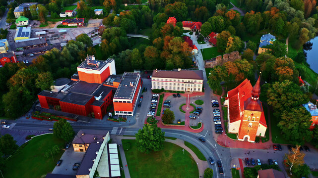 Aerial view of the town center of Valmiera featuring the historic St. Simon's Church, modern theater building, surrounding lush trees, and urban infrastructure in Latvia.