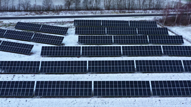 Aerial view of a solar farm with rows of photovoltaic panels installed in a snowy field in Latvia.