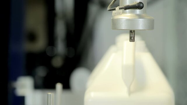 Closeup machine head descends plastic canister neck. Factory production line.