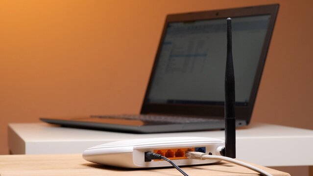 Wireless router featuring an antenna, ethernet cables, and a power cable connected to a laptop, illustrating home networking, internet access, and digital communication technology