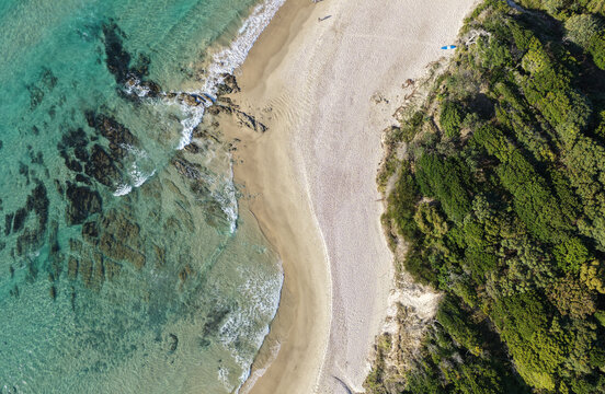 Aerial view of the coastline at Byron Bay, featuring turquoise water, rocky outcrops, sandy beach, and dense coastal vegetation in Byron Bay, New South Wales, Australia.
