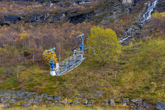 Aerial view of a metal cable car transport basket suspended over a steep, forested mountain slope with a waterfall in the background in Tafjord, More og Romsdal, Norway.