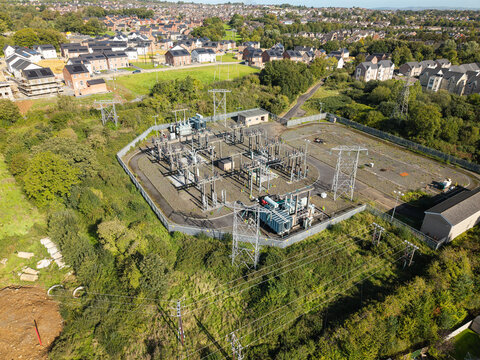 Aerial view of an electrical substation with transformers and power lines surrounded by green vegetation and residential housing in Lisburn, Northern Ireland, United Kingdom.