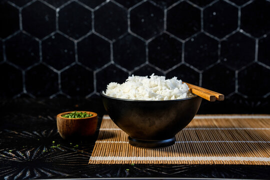 Jasmine white rice in a black ceramic bowl with chives and chopsticks 