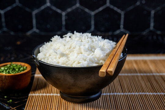 Jasmine white rice in a black ceramic bowl with chives and chopsticks 