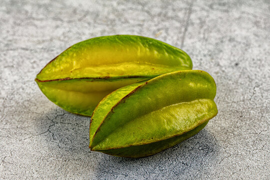 Two ripe carambola fruits with green and yellow ridged skin resting on grey stone surface, tropical star fruit close up, fresh food