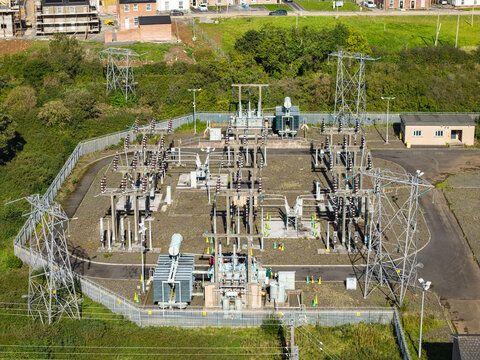 Aerial view of an electrical substation featuring transformers, power lines, and metal structures surrounded by green vegetation in Lisburn, Northern Ireland, United Kingdom.