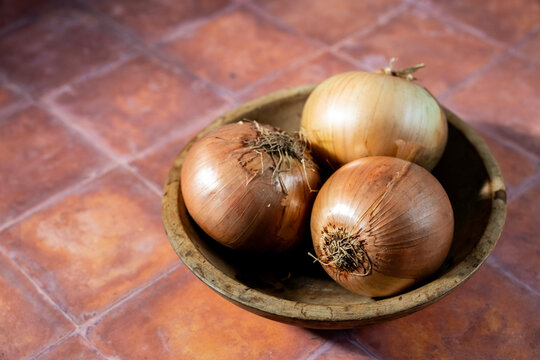 Yellow onions in a wood bowl on a tile surface 