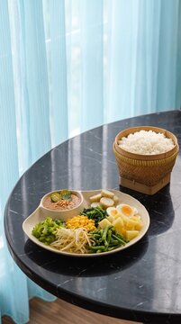 ​Traditional Indonesian gado-gado or pecel salad with assorted boiled vegetables, peanut sauce, boiled eggs, lontong, and rice in a bamboo basket