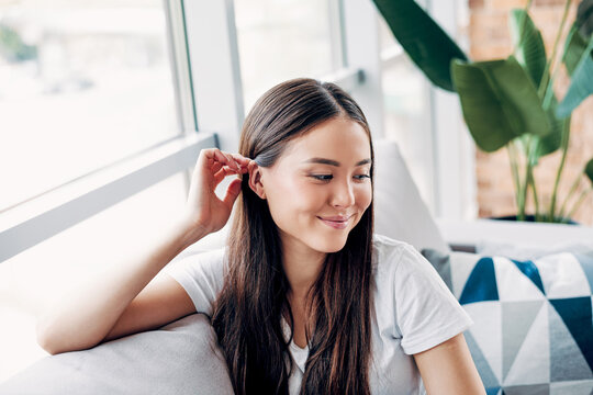 Young woman smiling and relaxed on a sofa at home by a bright window, casual portrait conveying comfort, calm and contentment