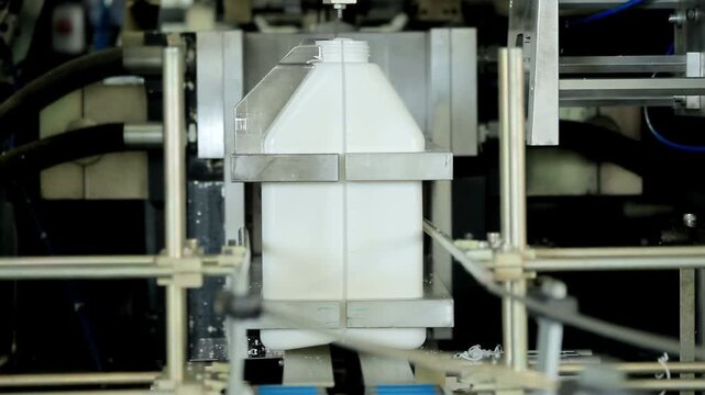 Canister blow molding machine factory. Plastic flash trimmed neck, clamp opens.