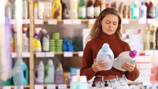 Selective young female buyer choosing convenient liquid laundry detergent in household goods shop 