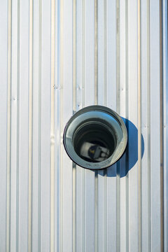 Dark round ventilation outlet casting shadow on corrugated steel wall.