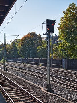 Railway signal post standing along multiple parallel train tracks with overhead catenary wires under a clear blue sky.