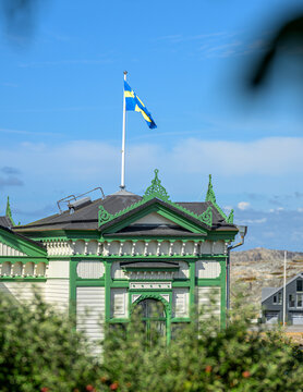 Swedish flag flying above ornate historic wooden coastal building.