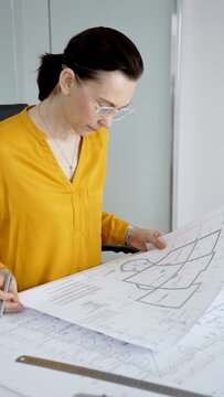 Architect woman reviewing and working on blueprints in office, designing new building construction plans, focusing on engineering details and planning project development