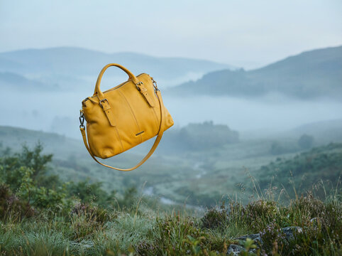 Mustard yellow leather tote suspended in midair above a misty mountain meadow