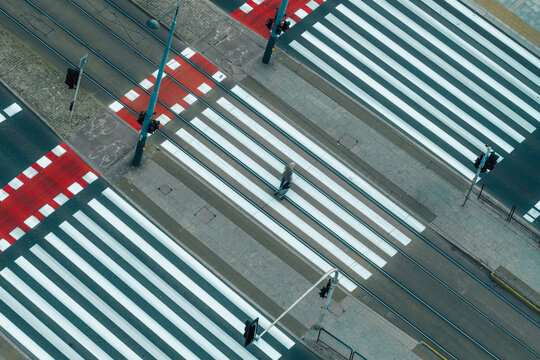 Aerial view of a pedestrian crossing with a person walking across the white stripes on a city street in Warszawa, Mazowieckie, Poland.