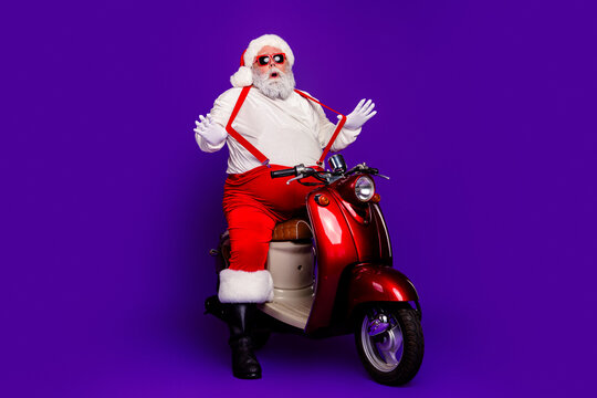 Santa Claus on a red scooter wearing sunglasses and suspenders against a vivid purple background enjoying a playful modern Christmas portrait