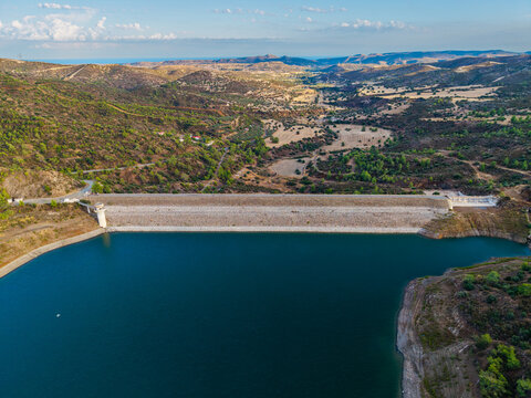 Aerial view of Dipotamos Reservoir with its dam wall and deep blue water surrounded by rolling hills and dry Mediterranean landscape in Dimos Lefkaron, Larnaca, Cyprus.