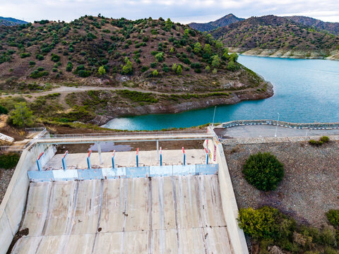 Aerial view of Dipotamos Reservoir featuring a concrete dam structure and turquoise water surrounded by hills and vegetation in Dimos Lefkaron, Larnaca, Cyprus.