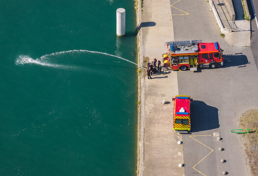 Aerial view of firefighters conducting a water rescue training exercise with fire trucks and hoses beside the Rhone river in La Voulte-sur-Rhone, Auvergne-Rhone-Alpes, France.