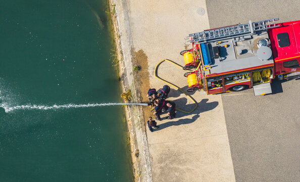 Aerial view of firefighters training with hoses and emergency equipment beside a river in La Voulte-sur-Rhone, Auvergne-Rhone-Alpes, France.