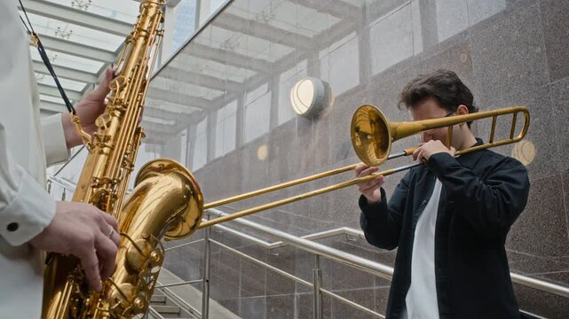 Caucasian young adult musicians playing saxophone and trombone outdoors, low angle shot. Ideal for urban music culture campaigns, entertainment promotions, or artistic youth lifestyle projects