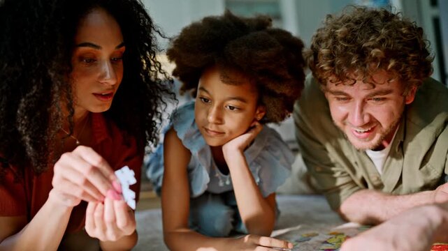 Family lying floor solving jigsaw puzzle. Close up multiracial parents kid home.
