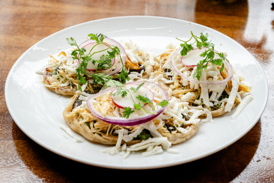 Traditional Mexican sopes topped with shredded chicken, onion, cheese, and cilantro on a white plate