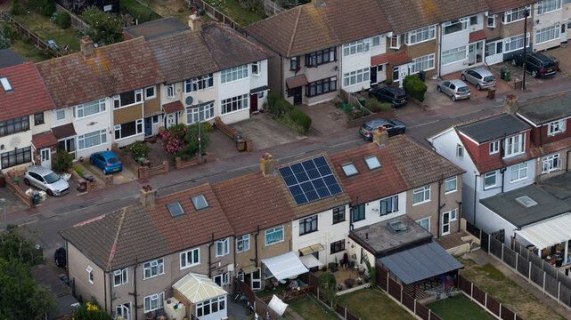 Aerial view of residential terraced houses with solar panels on rooftops, parked cars on the street, and private gardens in London, England, United Kingdom.