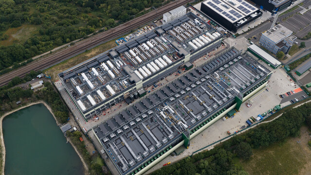 Aerial view of the NTT LON1B Data Centre featuring extensive rooftop HVAC units and industrial infrastructure situated near railway tracks and a pond in Dagenham, England, United Kingdom.