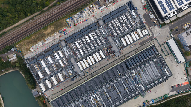 Aerial view of the NTT LON1B Data Centre featuring rows of cooling units and industrial infrastructure situated near railway tracks and a pond in Dagenham, England, United Kingdom.
