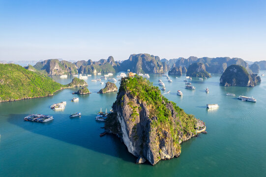 Aerial view of Ti Top Island in Ha Long Bay, featuring limestone karsts, turquoise waters, and numerous cruise ships under a clear blue sky, Ha Long, Quang Ninh, Vietnam.