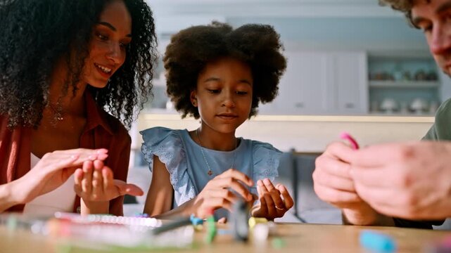 Girl rolling clay hands with parents home table. Multiracial family craft play.