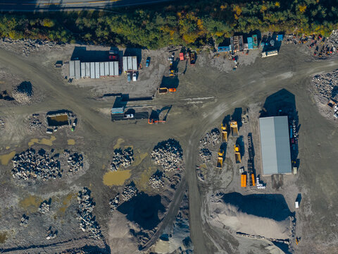 Aerial view of a construction site featuring piles of gravel, heavy machinery, and storage containers in Vestnes, More og Romsdal, Norway.