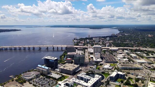 Drone pans right from Jacksonville riverfront buildings toward a sweeping highway interchange.
